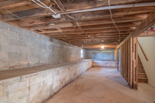 Empty basement with exposed concrete walls and wooden beams showing waterproofing potential